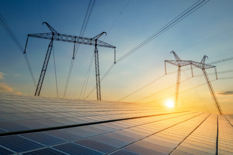 High voltage towers with electric power lines transfering energy from solar photovoltaic panels at sunset. Production of sustainable electricity concept